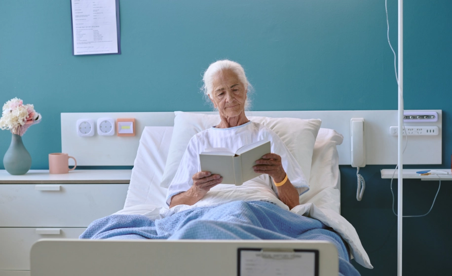 Oudere vrouw leest een boek in ziekenhuisbed