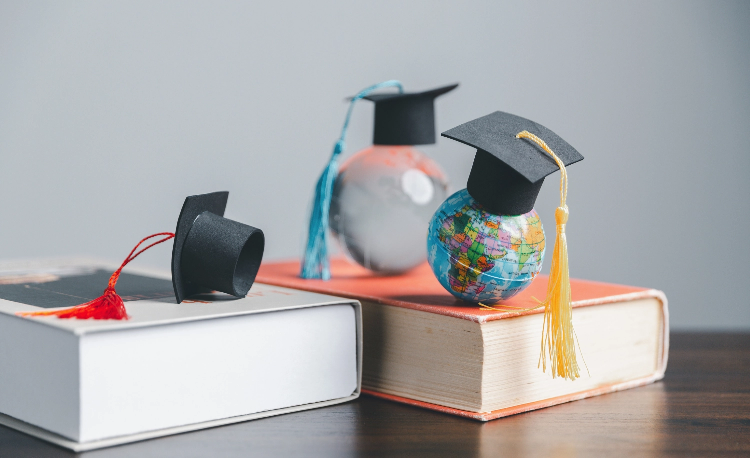 Afstudeerhoedjes liggen op dikke boeken en kleine wereldbollen met afstudeerhoedjes erop